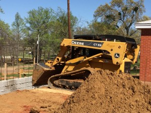 Sand is scooped down behind the foundation wall to fill the remaining hole in preparation for the forming and pouring of the slab. Photo: Barbara Wuthrich.